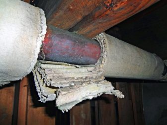 Pipe near rafters with damaged asbestos insulation