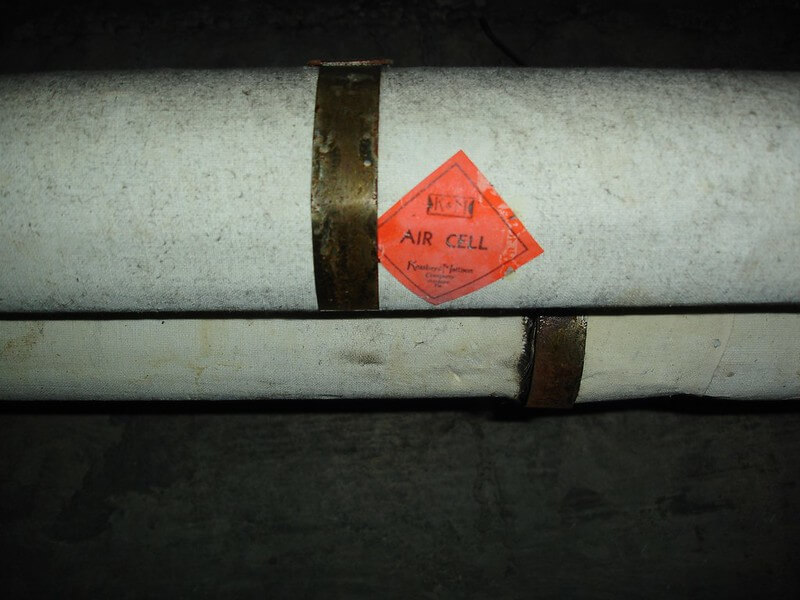 Asbestos pipe insulation labeled with a bright orange tag printed with information indicating 