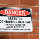 Close up photo of an industrial sign on a brick wall warning of asbestos