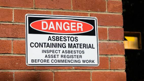 Close up photo of an industrial sign on a brick wall warning of asbestos