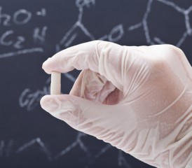 Gloved hand hold a pill in front of a chalkboard