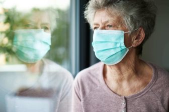 Woman with mask looking out a window