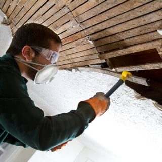 Man with mask tearing out old ceiling