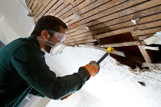 Man with mask tearing out old ceiling