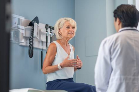 an older woman sits in a clinic exam room talking to her doctor