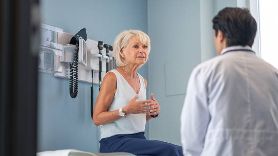 an older woman sits in a clinic exam room talking to her doctor