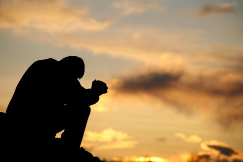 A silhouette of a man praying at sunset.