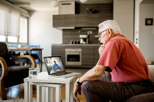 Older man looking at computer with image of doctor