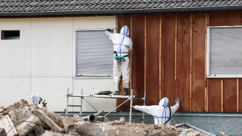 Professionals in protective suits remove asbestos on a wall