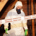 Man in protective clothing removing asbestos from building