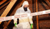 Man in protective clothing removing asbestos from building