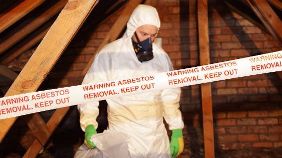 Man in protective clothing removing asbestos from building