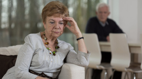 Elderly woman sitting in sofa looking serious with hand leaning on forehead.