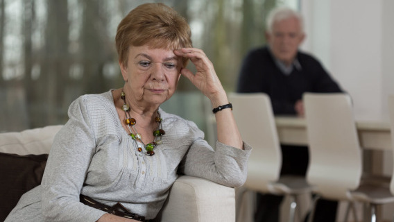 Elderly woman sitting in sofa looking serious with hand leaning on forehead.