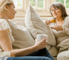 Two women sitting on couch holding coffee mugs