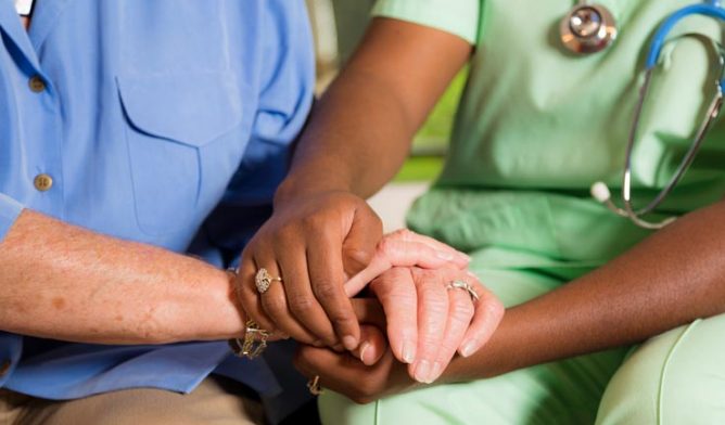 Home healthcare nurse holds senior woman's hands. Consoling. Kindness.