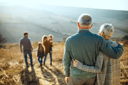 elderly couple embrace watching their daughter and her family