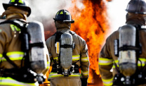 Three firefighters in gear facing flames