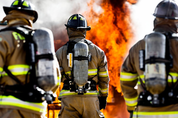 Three firefighters in gear facing flames