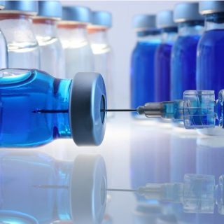 Laboratory bottles with blue content and a syringe