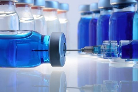 Laboratory bottles with blue content and a syringe