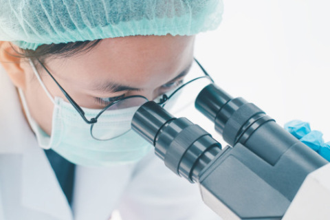Researcher studying cells under a microscope in a lab.