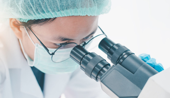 Researcher studying cells under a microscope in a lab.