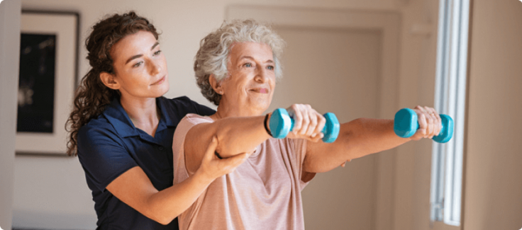 Old woman training with physiotherapist using dumbbells at home. Therapist assisting senior woman with exercises in nursing home.