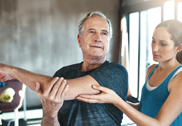 Older man stretching with a personal trainer in a gym