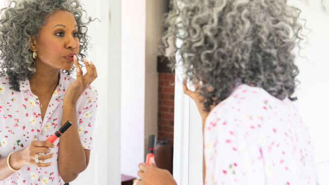 Older woman applying makeup in a mirror