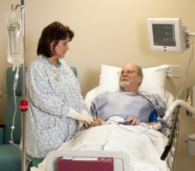 Female nurse assisting a male patient lying in a hospital bed