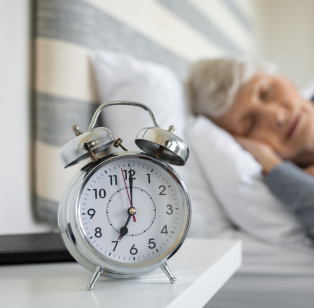 Older woman sleeping next to an alarm clock
