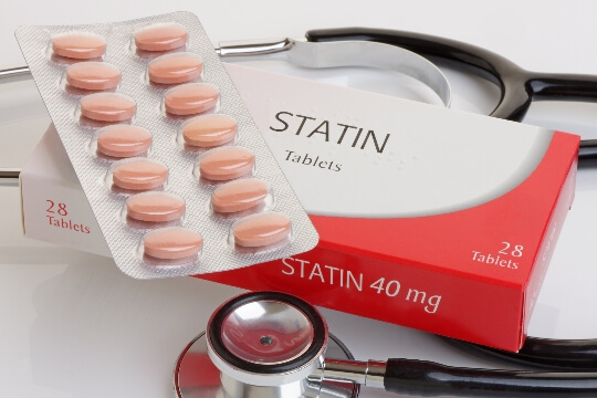 Pink pills in plastic with box that says statins and a stethoscope