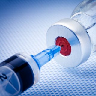 Syringe poking into a vaccine vial