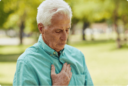 Older man holding his chest while sitting in a park