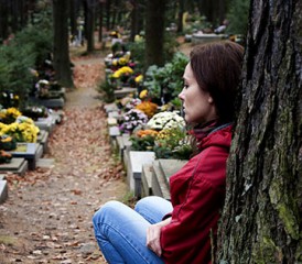 Woman grieving against a tree in a cemetery