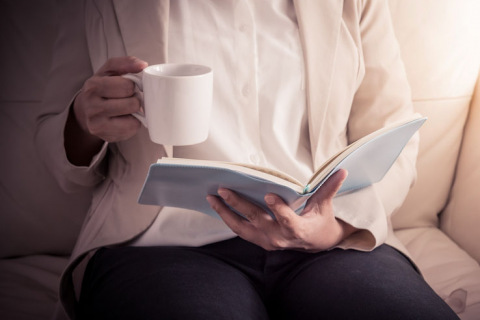 Woman relaxing on sofa and reading book while holding cup