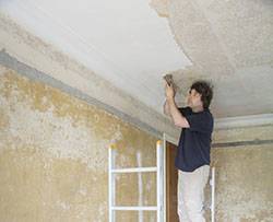 Homeowner scraping popcorn ceiling texture in a house