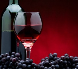 Bottle and glass of red wine with grapes in foreground Bottle and glass of red wine with grapes in foreground