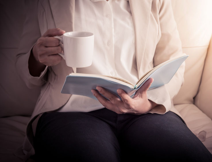 Woman relaxing on sofa and reading book while holding cup Woman relaxing on sofa and reading book while holding cup